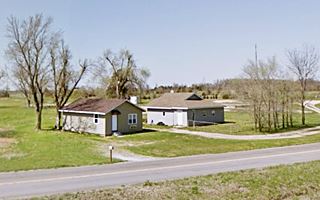 two homes with gabled roofs by highway in a field