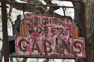 John’s modern cabins neon sign, Route 66 Newburg MO rusty peeling motel neon sign partly hidden in the trees