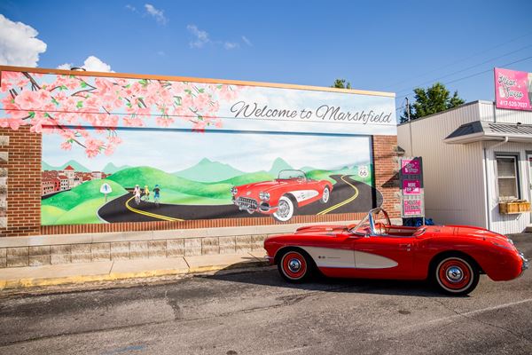 mural painted on a wall depicting a winding Route 66, cherry blossoms, and a red convertible and a city. Red convertible is parked facing the mural