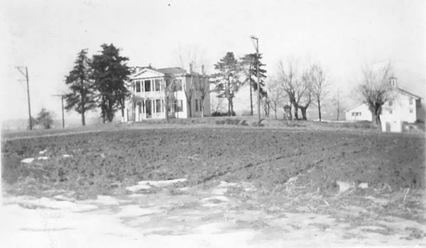 black and white photo of a two story house with columns, portico in a field