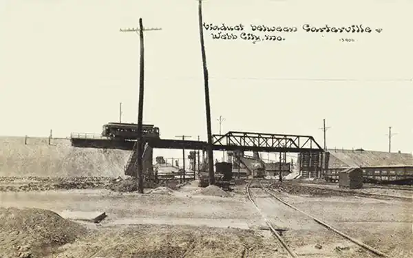 1930s black and white photo of the Electric streetcar atop a bridge overpass, railroad below.
