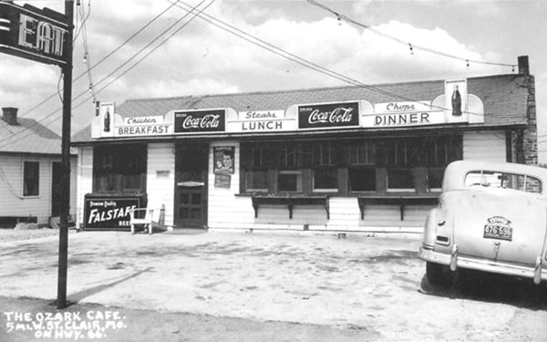 black and white 1940s postcard of gable roof cafe, neon sign, and car