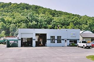 oblong box 2 bay concrete block 1950s gas station, forested hill beyond