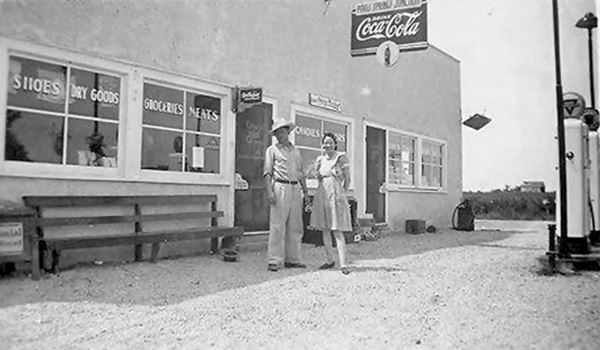 black and white 1940s photo man and woman by gas pumps in front of a store