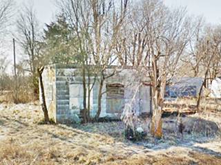 trees surround ruins of a box-like former gas station