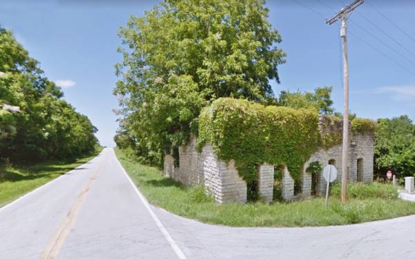old vacant overgrown building with rough stone walls and ivy on a corner by Route 66