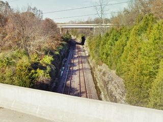 deep cut, with trees on both sides and railroad tracks running along it, seen from Route 66 bridge, I-44 in the distance spans the cut