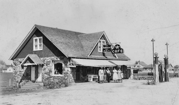 black and white picture ca. 1940 gable roofed stone faced gas station and people