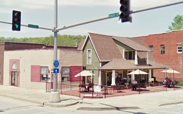 color view of former gas station on corner with parasols and tables