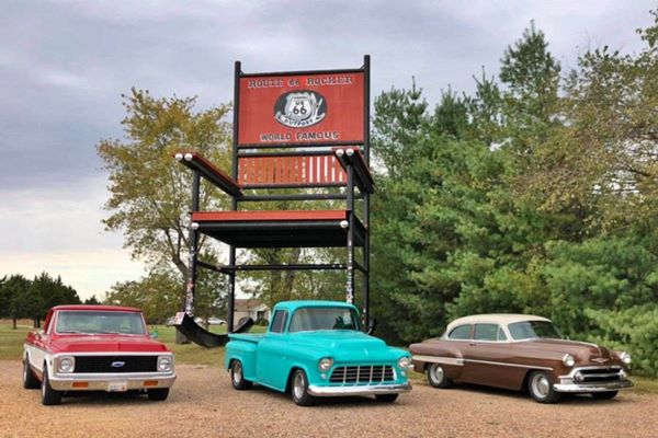 giant red rocking chair and three vintage cars dwarfed by it