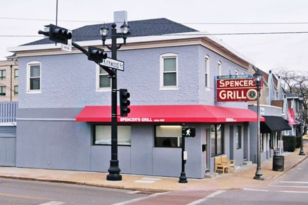 two story gray, gable roof building with vintage neon sign: Spencer’s grill