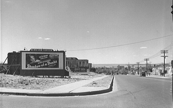 Looking west down Central Avenue into the business district, Feb. 1943, Collier, John Jr. black and white photo, buildings in the distance, highway to the right, gas station beyond. Movie sign to the left, Hospital and underpass in the distance