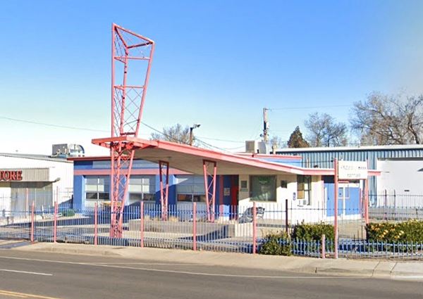 triangular shaped canopy, with a steel pole supporting its snub tip: a former Phillips 66 gas station seen from US66. Steel fence surrounds it. Two service bays to the left