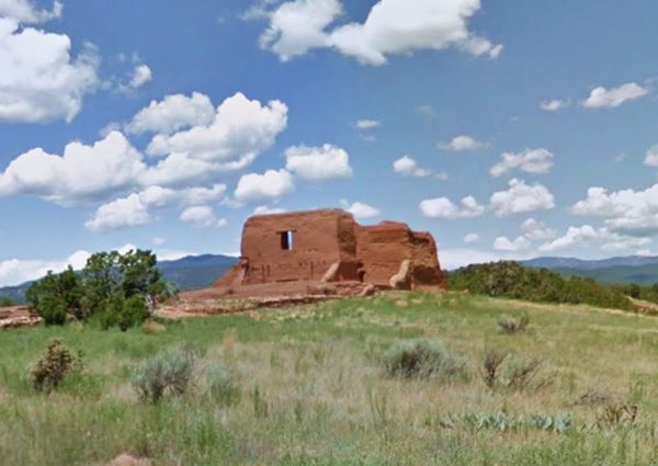 color, grassy field, some trees, and a reddish-brown building with thick adobe walls: ruins of a Colonial Church in Pecos Pueblo
