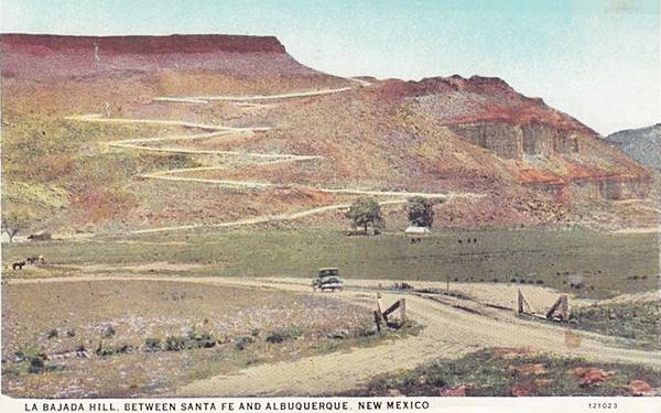 color postcard 1920s, car heads north towards steep hill with zig-zag roadway climbing it