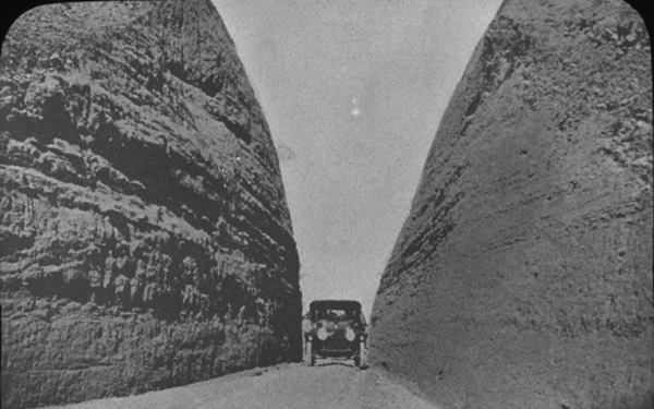 black and white, car in a narrow deep cut in a hill, 1920s
