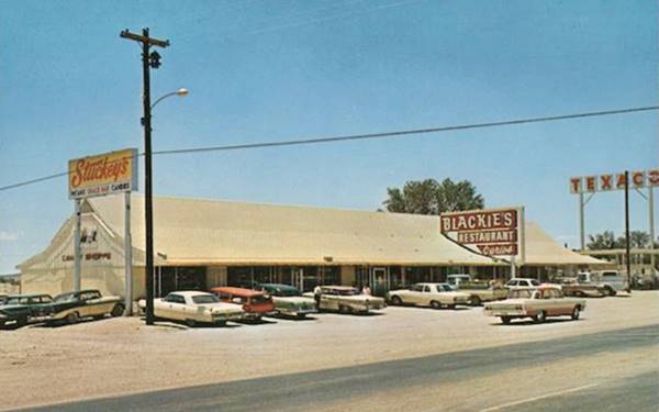Blackie’s cafe in the 1960s, US66 Moriarty color 1960s postcard: long cafe, cars parked in front of its windows, neon sign with name, Texaco gas station to the right