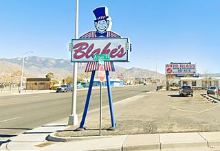 Blakes Lotaburger sign on a corner: man-shaped sign, with red and white striped jacket, bow tie and top hat with two slender blue steel legs, BLAKE’S written in red on a white sign held by the man-sign