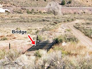 cocrete abutement and wood deck bridge, paddock horse beyond, road to the right and railroad in the distance on embankment