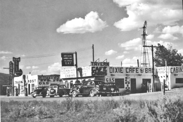 black and white photo 1940s cars, a cafe, trading post neon signs, gas pumps and windmill seen from US66 that runs in front of them