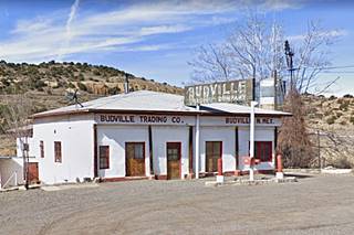 Budville Trading Co. Hipped roof former trading post, gas pumps island, and faded sign. Hills beyond