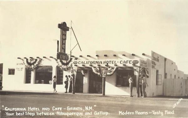 black and white, people by a Cafe and Hotel with vigas protruding out of facade. Adobe Pueblo style building. Neon signs