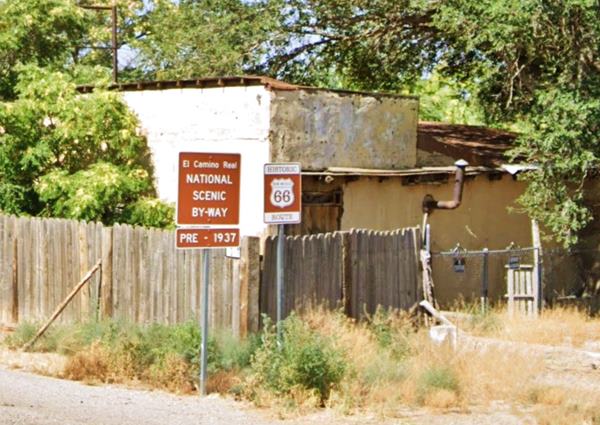 color: brown sign with white letters marks Historic Route 66 alignment and the Camino Real, old house behind, with trees