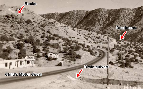 black and white 1930 photo: winding US66, car, trading post, steep sloped hills and arid setting, bushes