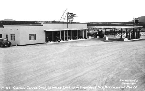 black and white postcard of a cafe, single floor, box shaped, Phillips 66 station -righit- with flat canopy, hills in the distance, sign reads: COMER
