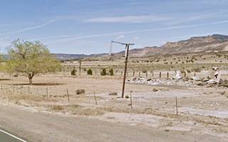 Cuberon Motel ruins Cubero NM vacant lot, rubble behind, hills beyond some trees and a vacant sign and signpost ruins of a motel on Route 66