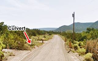 Culvert on Old US66 Canyoncito color, dirt road, concrete culvert, hills in the distance, shrubs and low trees on both sides