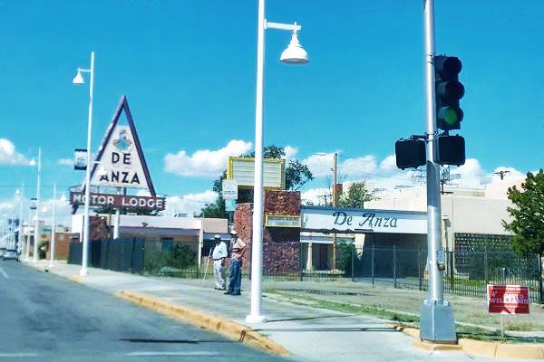 View of the De Anza Motor Lodge neon sign, triangular to the right, Route 66 on the left, two men on the sidewalk