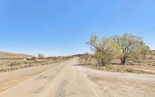 looking east along Route 66 in a hilly arid area, with some trees to the right and homes to the left in Defiance New Mexico