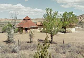 Defiance Trading Post bldg 2012 hogan shaped sandstone building, with conical roof dome and trees, arid setting, annex building to the right