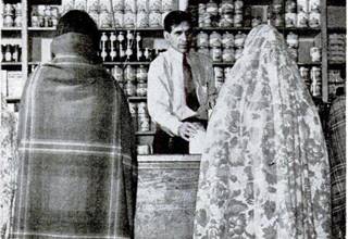1943 Life Magazine: Domingo Trading Post black and white, 1943 man selling goods to two native women at the counter in a trading post, canned goods on shelves behind him