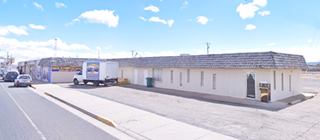 Encanto Motel nowadays US66 Grants NM units of a motel facing a parking area. Route 66 to the left, stores further along the highway to the left
