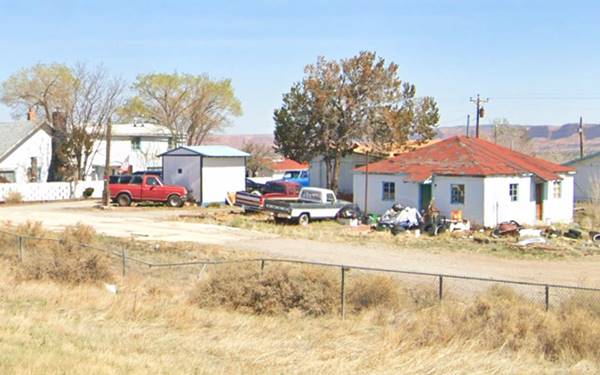 group of buildings and some vehicles, trees, yellow grass. In front passes the old Route 66, former trading post