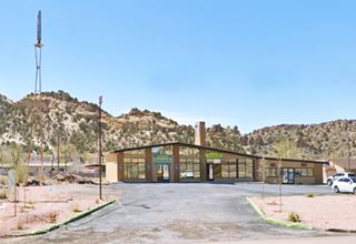 glass faced building, gable roof, glass transoms, hills behind, steel signpost right, paved drive, seen from US66