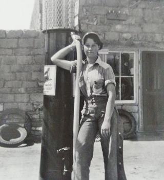 Genta Rice at her father’s Texaco Station in San Fidel US66 NM young woman (Genta Rice) in overall by 1930s gas pump, adobe building behind her, black and white