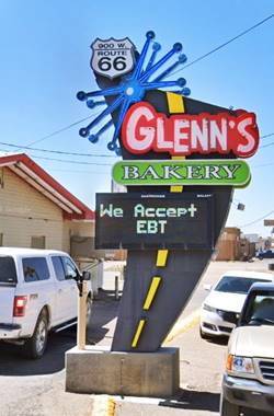modern neon sign with US66 shield, blue star and the word GLENN’S in white letters with red border and BAKERY in white on green, black angled pole with yellow dashed line like a highway