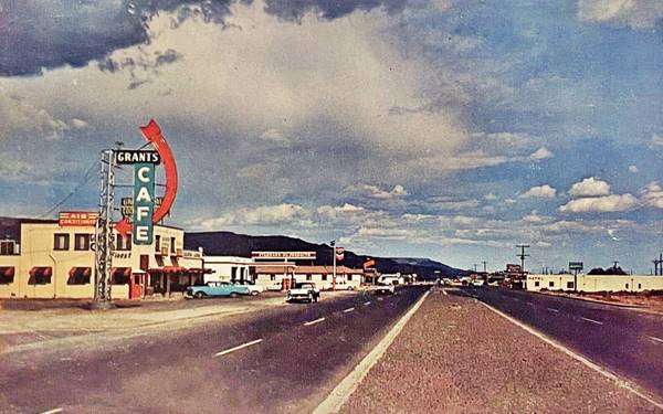 color 1950s. Looking east along US66: left: Grants Cafe and red-blue neon sign, Chevron Station. Motel. Left: motel. Cars on divided avenue