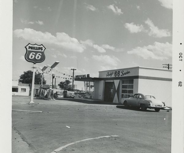 black and white view of a Phillips 66 gas station: pumps, sign, logo, office, cars from 1962