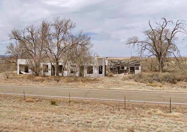 abandoned building among the trees, Route 66 passes in front. Overgrown shrubs, empty windows in a single story concrete block building