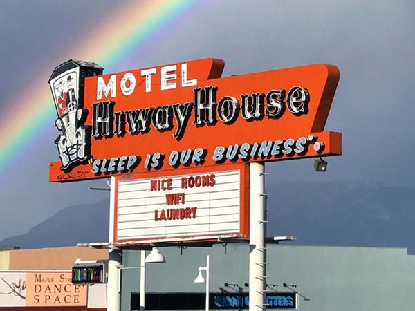 rainbow and dark skies behind a red neon sign, with white letters: MOTEL HIWAY HOUOSE "SLEEP IS OUR BUSINESS"