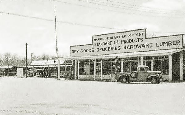 black and white woodframe store with sign on its facade, pick up truck parked on dirt parking area