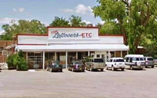 Huning Store in 2016 woodframe white store with verandah, trees benhind, cars parked in front of it