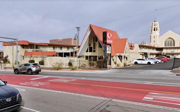 Two story motel in the background with a flat roof, false red mansard facing US66, and a Chalet with steep gable roof as the office by neon sign. Church to the right in the background