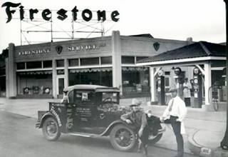 1931 Firestone Service Store with Jules Allen black and white photo, Firestone store, gas pumps under tiled canopy, two men by a 1930s truck, dog sitting on it