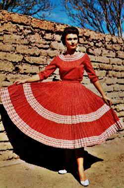Justin’s Shop postcard 1950s woman in a red lace Fiesta Dress, color photo c.1950s, adobe brick wall behind her
