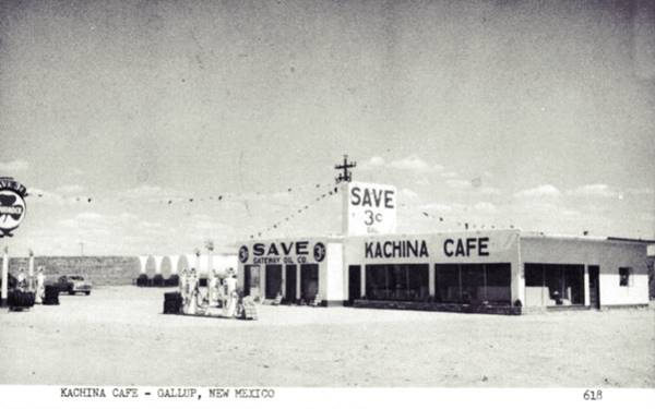 1950s black and white flat roof building with vertical extension on roof, Shamrock gas sign, 3 pumps and car. CAFE written on building, tanks to the left